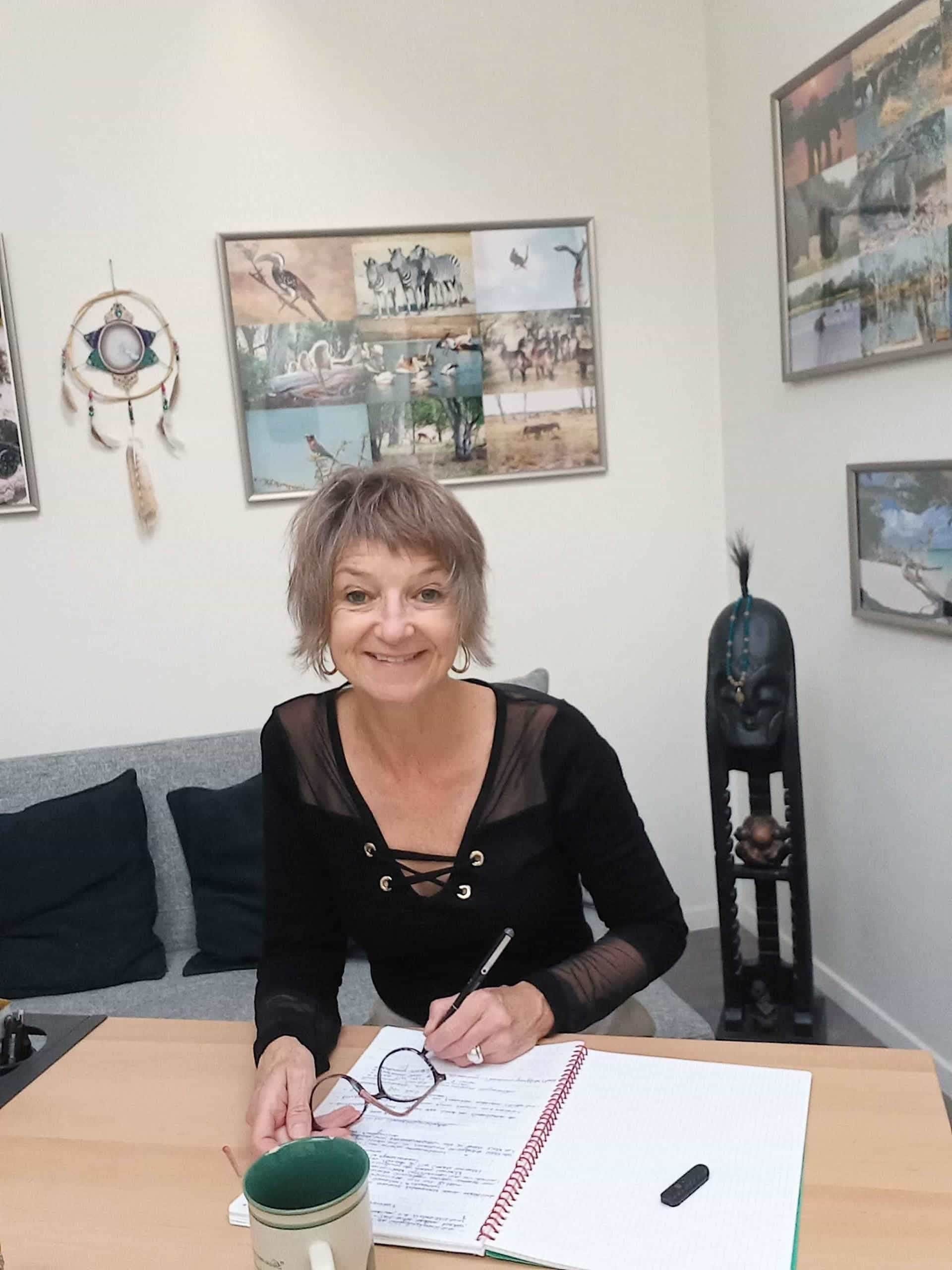 Katja Rehse sitting at her desk, writing in a notebook and smiling at the camera.