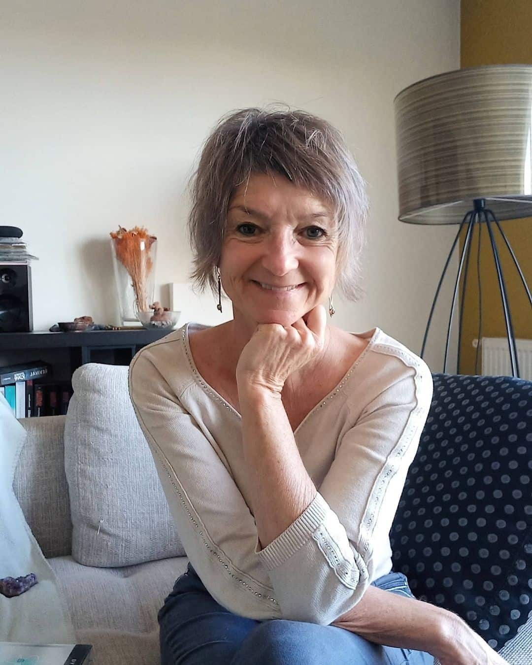 Katja Rehse sitzt mit übereinandergeschlagenen Beinen auf einem hellgrauen Sofa, hat eine Hand unter dem Kinn und lächelt.