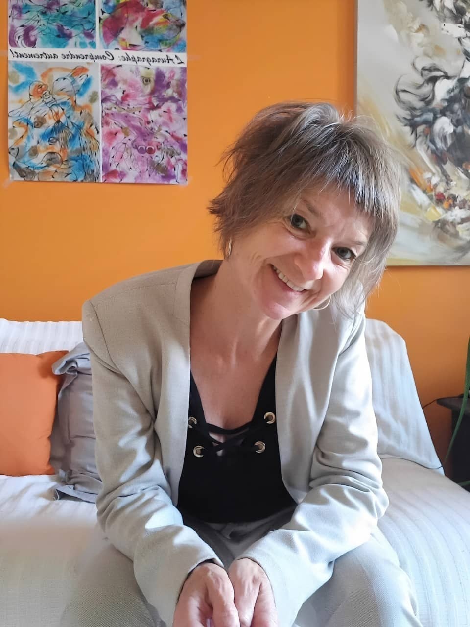 Katja Rehse sitting on a white sofa in her consultation room, smiling with her hands gently joined.