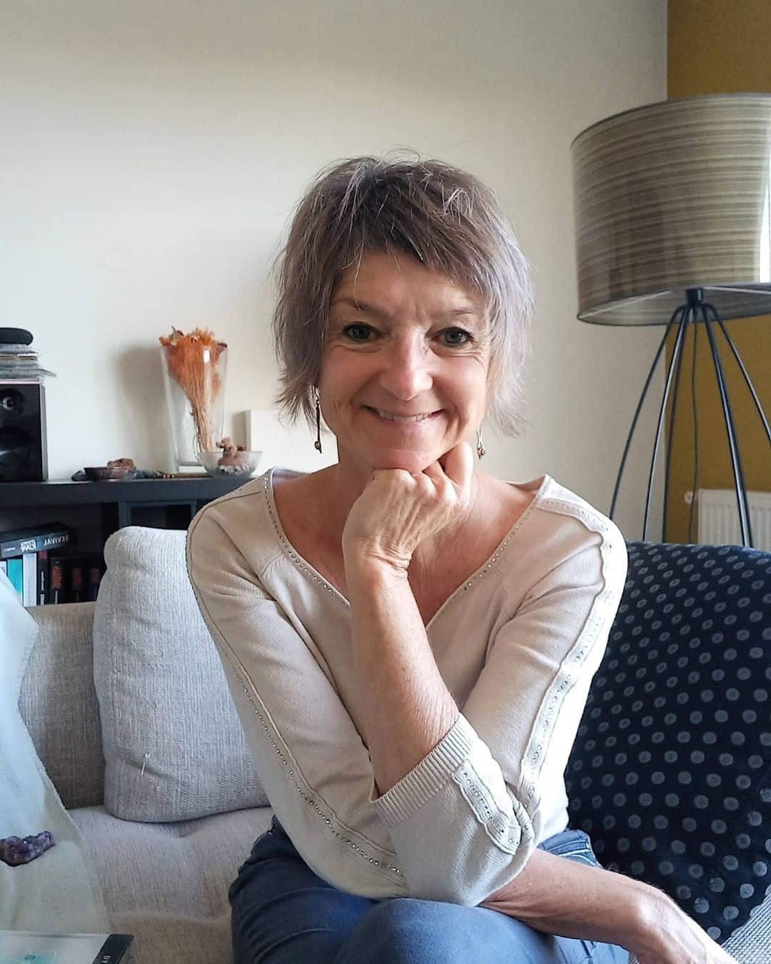 Katja Rehse sitting on a light grey sofa with her legs crossed, one hand under her chin and smiling.